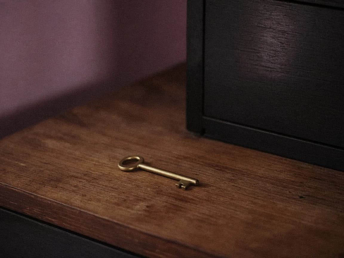 A brass key on a teak counter beside a closed cabinet, mauve last light.